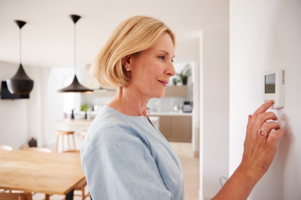 Older woman adjusting the air conditioner on her newly replaced HVAC unit in her home