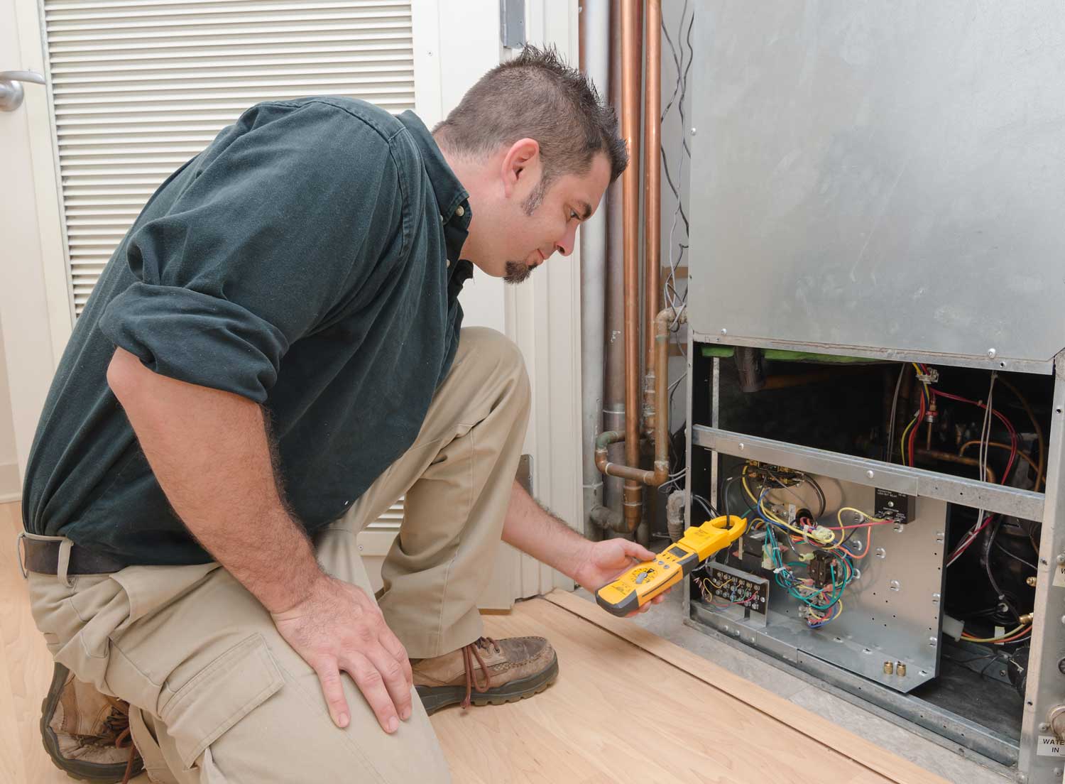 HVAC technician testing ampage on air conditioning unit during repair