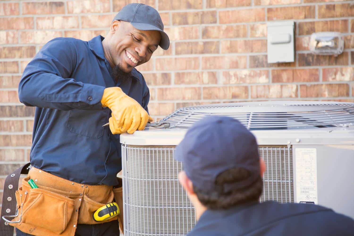 two HVAC technicians repairing an external unit